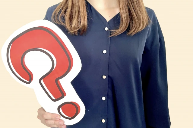 はてなマークを持った、紺色の服を着た女性
